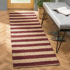 May include: A rectangular runner rug featuring a repeating horizontal striped pattern in alternating bands of natural tan jute and deep burgundy red. The rug has a textured, woven surface and is laid flat on a light-colored wooden floor.