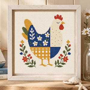 May include: A framed cross-stitch of a colorful chicken. The chicken has a blue and yellow patterned body with white flower accents. Red, yellow, and green floral elements surround the chicken, all set against a cream-colored background.