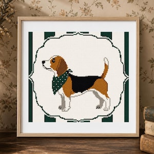 May include: A framed cross-stitch picture of a beagle dog with brown, black, and white markings, wearing a green polka-dot bandana. The dog is set against a white background with a decorative border and green vertical stripes. The frame is wood-toned.