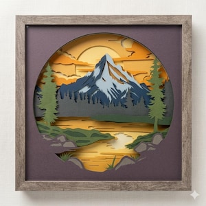 May include: A framed paper art piece depicting a mountain landscape. The artwork features a mountain with blue and white accents, a lake, and trees, all set against a sunset sky with orange and yellow hues. The frame is a neutral gray.