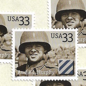 May include: A black and white postage stamp featuring a portrait of Audie L. Murphy wearing a military helmet. The stamp includes the text USA 33, the name Audie L. Murphy, and a square emblem with three diagonal blue stripes on a white background.