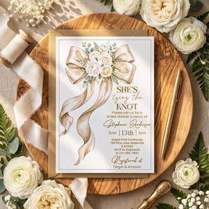 May include: A rectangular bridal shower invitation card featuring a watercolor illustration of a large beige ribbon tied into a bow with white flowers and green foliage. The text reads: She's tying the KNOT, Stephanie Anderson, June 13th, 4pm.
