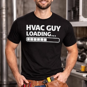 May include: Black crew neck t-shirt with the text "HVAC GUY LOADING..." in white. The shirt features a loading bar graphic. The person in the image is wearing a brown leather tool belt and blue jeans.