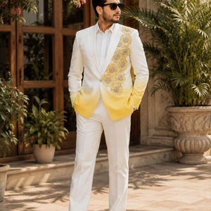 May include: A white blazer with a yellow ombre hem and floral embroidery on the left lapel, paired with a white button-down shirt, white trousers, and white sneakers. The blazer features a notched lapel and a single-button closure at the front.