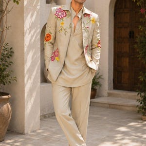 May include: A light beige suit consisting of a blazer and matching trousers. The blazer features vibrant floral embroidery in shades of red, pink, and yellow on the lapels and sleeves. A plain light beige shirt is worn underneath the blazer.