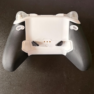May include: A black and white gaming controller with textured grips. The controller has a white centre section with black joysticks and buttons. The top has clear plastic accents.