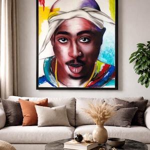 May include: A framed portrait of a person with a white head covering and a gold chain. The artwork features a colorful background with yellow, blue, and red hues. The person's expression includes a tongue sticking out.