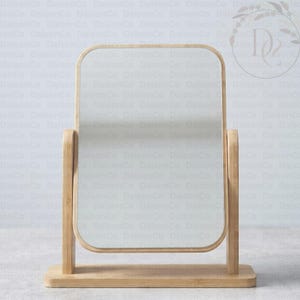 May include: A rectangular tabletop mirror with a light-toned wooden frame and stand. The mirror features rounded corners and is mounted on two vertical wooden supports attached to a flat, rectangular wooden base, allowing for a tilting motion.