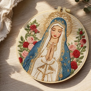 Può includere: Un telaio da ricamo circolare contenente un pannello in tessuto con un dettagliato ritratto ricamato di una figura con gli occhi chiusi e le mani giunte in preghiera, che indossa un velo blu e bianco, circondato da rose rosse e rosa.