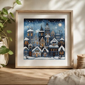 Pode incluir: Uma obra de ponto cruz emoldurada retratando uma vila de inverno à noite. A imagem apresenta edifícios em tons de azul com telhados cobertos de neve, janelas amarelas brilhantes e um céu estrelado com lua cheia. Uma silhueta de veado na neve.