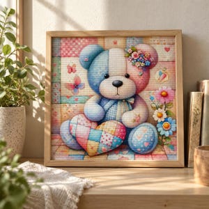 Peut inclure: Une peinture diamant carrée dans un cadre en bois clair représentant un ours en peluche au design bicolore bleu et rose. L'ours tient un cœur en patchwork multicolore, orné de petites fleurs et de papillons sur un fond à motifs quadrillés.