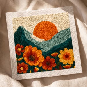 May include: A square, framed textile art piece featuring a landscape scene. The artwork depicts a vibrant orange sun setting behind teal and green mountains. The foreground showcases orange and yellow flowers. The piece is framed in a neutral-toned fabric.
