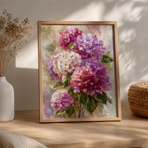 May include: A framed oil painting on canvas depicting a cluster of hydrangea flowers in shades of pink, purple, and white. The artwork features thick, textured brushstrokes and deep green leaves, all encased in a simple light-toned wooden frame.