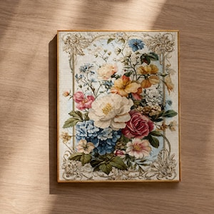 May include: A framed floral cross-stitch artwork. The artwork features a bouquet of colorful flowers, including roses, hydrangeas, and other blooms in shades of pink, blue, yellow, and white. The frame is a warm gold color, and the background is a light cream color.