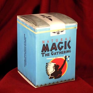May include: A light blue rectangular box with a white top seal. The front features the text "NATURAL MAGIC THE GATHERING" above a graphic of a silhouette figure with a headdress holding a sword against a red and yellow circle background.