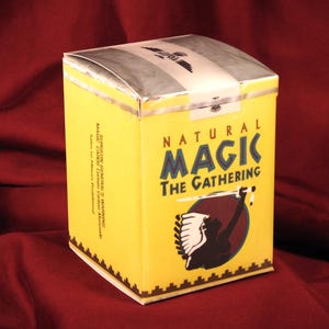 May include: A rectangular yellow box with the text Natural Magic The Gathering printed on the front. The design includes a graphic of a silhouette figure holding a sword. The side of the box features a Surgeon General's warning in black text.