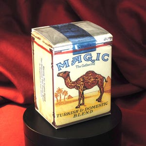 May include: A vintage box with the words "MAGIC The Gathering" and a camel illustration. The box has a cream background with blue and white accents. The text "TURKISH & DOMESTIC BLEND" is also visible.