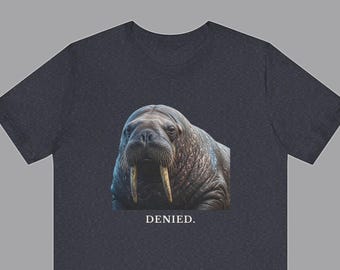 May include: A dark heather gray t-shirt featuring a realistic photographic print of a walrus with prominent tusks and whiskers. Below the walrus, the word DENIED. is printed in a clean, white, serif font centered on the chest of the garment.