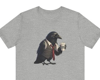 May include: A heather grey t-shirt featuring a graphic of a black raven wearing a white collared shirt, a grey waistcoat, and a red necktie. The raven is holding a white coffee cup with the text "CHAOS COORDINATOR" printed on the side of the cup.