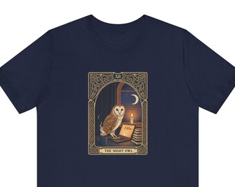 May include: A navy blue t-shirt featuring a rectangular graphic of a barn owl sitting at a desk with a laptop, a stack of books, a candle, and a mug. The graphic is framed in a gold border with the text XII and THE NIGHT OWL at the bottom.