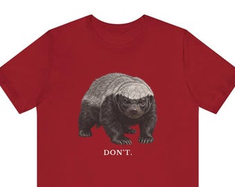 May include: A dark red short-sleeved t-shirt featuring a detailed illustration of a honey badger in shades of gray and white. Below the animal, the word DON'T. is printed in white capital letters with a period at the end of the text.