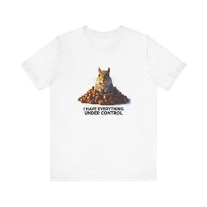 May include: White t-shirt with a graphic of a squirrel peeking out from a pile of nuts. The text "I HAVE EVERYTHING UNDER CONTROL" is printed below the squirrel. The squirrel has a surprised expression.