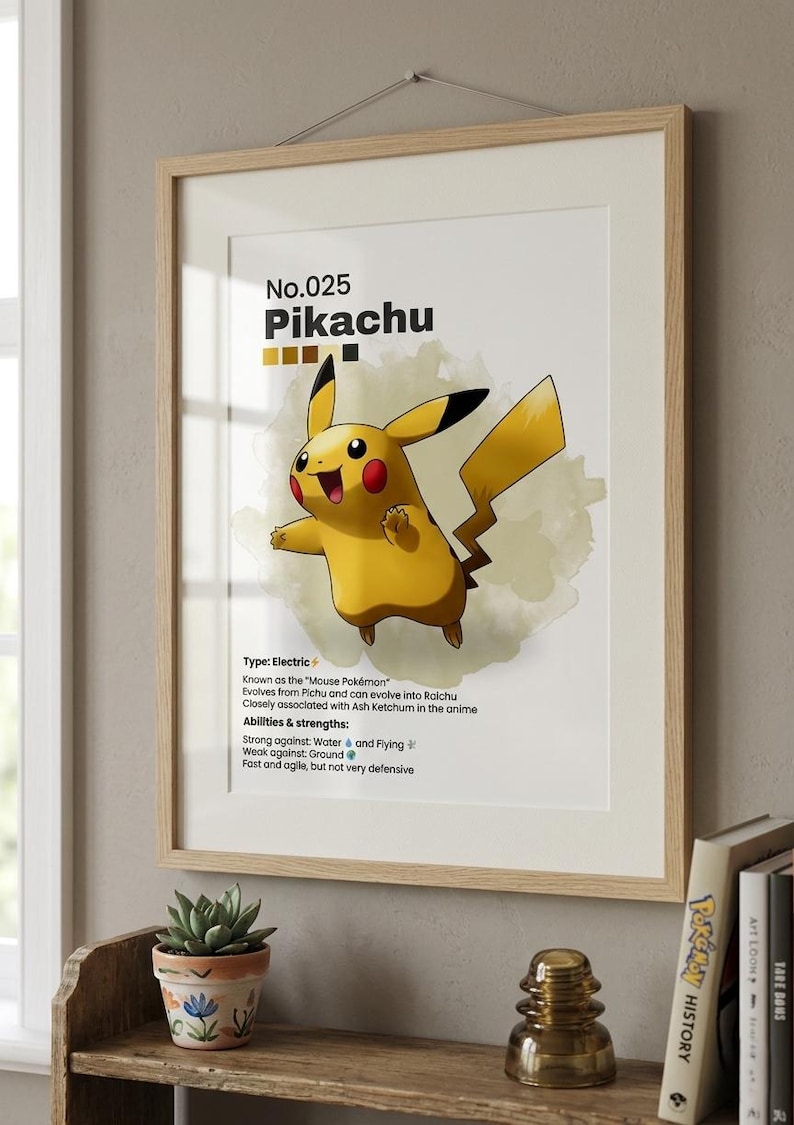 May include: A framed print featuring Pikachu, a yellow electric-type Pok&eacute;mon. The artwork includes the Pok&eacute;mon's number, name, and a description of its abilities. The print is in a light wood frame and is displayed on a shelf with books and a small potted plant.