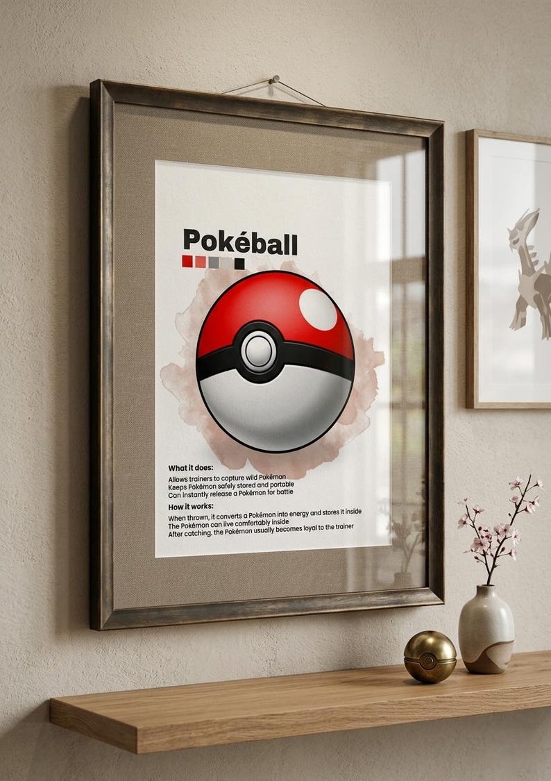 May include: Framed print featuring a red, white, and black Pok&eacute;ball design. The print includes the word "Pok&eacute;ball" at the top and text describing its function. The artwork is displayed on a wooden shelf with decorative items.