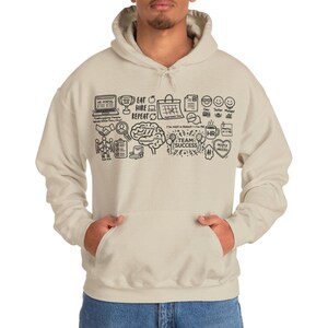 Peut inclure: Un sweat à capuche beige avec une impression graphique noire composée de diverses icônes de bureau et de textes comme "EAT HIRE REPEAT", "TEAM SUCCESS", "HR PORTAL" et "I'm Not a Robot - I'm HR", incluant des dessins de cerveau, trophée et calendrier.