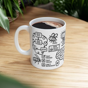 May include: A white ceramic mug filled with black coffee, featuring black line art graphics related to software development, including a bug cycle, a 404 bug not found box, a sad computer icon, and text labels like test passed and test failed.