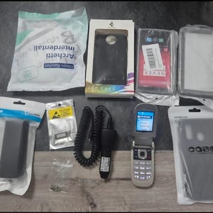 May include: A collection of items including a pack of Filippo Bianchini interdental brushes, a Spigen SGP case box, two clear phone cases, a black car charger with a coiled cord, a silver flip phone, and various small electronic accessories in bags.