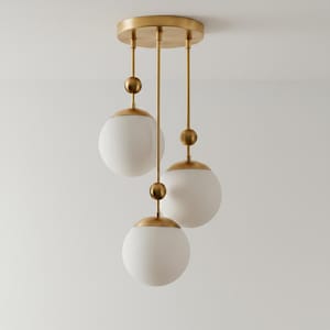 May include: A modern pendant light fixture with three white globe shades suspended from a gold-toned ceiling mount. Each globe is accented with gold-toned hardware and a decorative sphere. The fixture is designed for interior lighting.