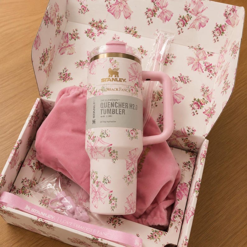 May include: A white and pink floral Stanley Quencher H2.0 tumbler with a pink handle, inside a matching floral box. The tumbler has the text "QUENCHER H2.0 TUMBLER" and "SHACK FANCY". The box contains a pink bag and a pink strap.