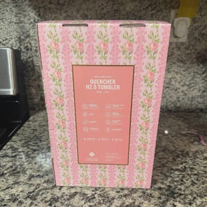Pu&ograve; includere: Una scatola rosa a motivi floreali per un bicchiere Quencher H2.0. La scatola ha un'etichetta rettangolare con il nome e le caratteristiche del prodotto. La scatola &egrave; decorata con un motivo ripetuto di rose rosa e foglie verdi.