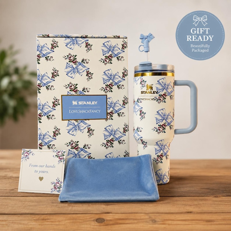 Pu&ograve; includere: Un set regalo con un bicchiere Stanley a fantasia floreale bianca e blu con manico, una scatola abbinata, un astuccio in velluto blu e un biglietto. Il bicchiere ha una cannuccia blu e dettagli dorati. La scatola e il bicchiere riportano la scritta "LOVESHACKFANCY".