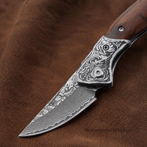Puede incluir: Una navaja plegable con una hoja de acero de Damasco con un patrón ondulado distintivo. El refuerzo de metal está decorado con intrincados grabados de volutas. El mango está hecho de madera marrón oscura con veta visible y un tornillo plateado.