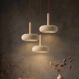 Könnte beinhalten: Drei Pendelleuchten mit schirmförmigen Lampenschirmen und Holzdetails. Die Leuchten hängen an braunen Kabeln und erzeugen ein warmes Licht. Das Design ist minimalistisch und modern, geeignet für die Inneneinrichtung.