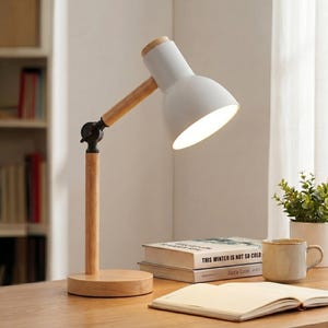May include: A white desk lamp with a wooden arm and base. The lamp has a round, white lampshade and a wooden accent at the top of the shade. The lamp is turned on, illuminating the desk. The lamp is approximately 12 inches tall.
