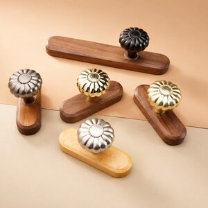 May include: A collection of decorative cabinet pulls with flower-shaped knobs. The knobs are in silver, gold, and black finishes, mounted on wooden rectangular bases. The wood tones vary from light to dark brown.
