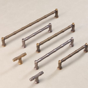 May include: A collection of cabinet hardware featuring a bamboo design. The handles and knobs are in various metallic finishes, including bronze and silver. The hardware is designed for furniture and cabinetry.