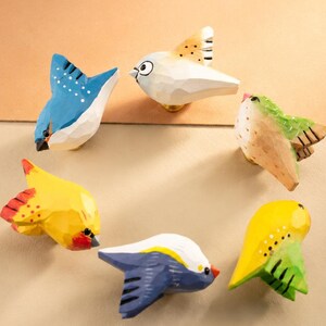 Puede incluir: Un conjunto de seis pomos para cajones de madera tallada a mano con forma de pájaro. Cada pomo presenta un esquema de color único que incluye azul, blanco, amarillo y verde, con superficies facetadas y detalles pintados que representan varias aves.