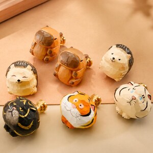 May include: A collection of seven small, hand-carved wooden animal drawer knobs. The set includes figures of hedgehogs, tigers, and capybaras, each featuring a smooth, polished finish and a gold-toned metal screw base for attachment to furniture.