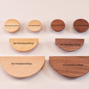 Puede incluir: Una colección de herrajes de madera para muebles en tonos claros y oscuros. El conjunto incluye dos pomos circulares, dos tiradores semicirculares y dos grandes tiradores en forma de media luna. Cada pieza lleva el texto No1HardwareShop.