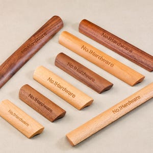 Puede incluir: Una colección de siete tiradores de madera para armarios de distintas longitudes, con un perfil curvado y un acabado liso. Cada pieza está fabricada en madera clara u oscura y lleva grabado a láser el texto No.1Hardware en la parte frontal.