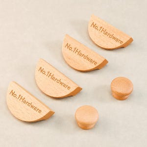 Può includere: Quattro maniglie per cassetti in legno chiaro di forma semicircolare e due piccoli pomelli rotondi in legno. Ogni maniglia semicircolare è incisa con il testo No.1Hardware in un carattere scuro. Gli oggetti hanno una finitura in legno naturale.