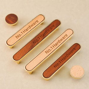 May include: Four rectangular cabinet pulls and two circular knobs featuring a gold metal frame with a wood inlay. Each rectangular pull is engraved with the text No.1 Hardware. The wood grain varies in colour from light to dark brown.