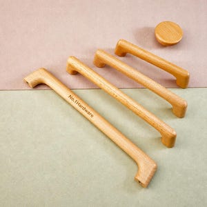 May include: Three light-coloured wooden cabinet handles of varying lengths and one circular wooden knob. The longest handle features the text No.1Hardware engraved on its surface. Each piece has a smooth finish and a natural wood grain pattern.