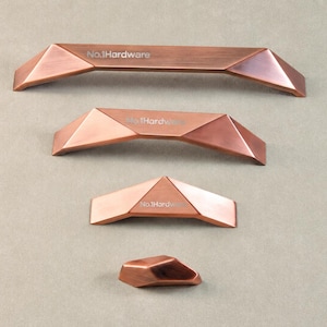 May include: Four copper-colored cabinet pulls with a faceted, geometric design arranged in descending order of size. Each pull features a brushed metallic finish and the text No.1Hardware engraved on the top surface of the three larger pieces.