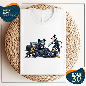 May include: White t-shirt featuring a cartoon image of Mickey Mouse, Goofy, Donald Duck, and Pluto with a Formula 1 race car. The characters are dressed in racing attire. The shirt is displayed on a woven surface.