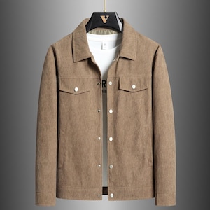 May include: A tan corduroy jacket with a button-up front, two chest pockets, and a collared neckline. The jacket is hanging on a black hanger. A white t-shirt with the word "R" is visible underneath.